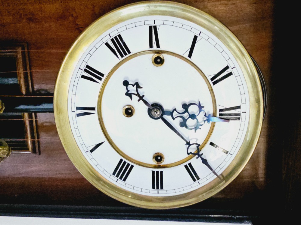 A nineteenth-century walnut Vienna regulator wall clock featuring three suspended brass weights, turned columns, carved finials, and a white enamel dial with Roman numerals. View II