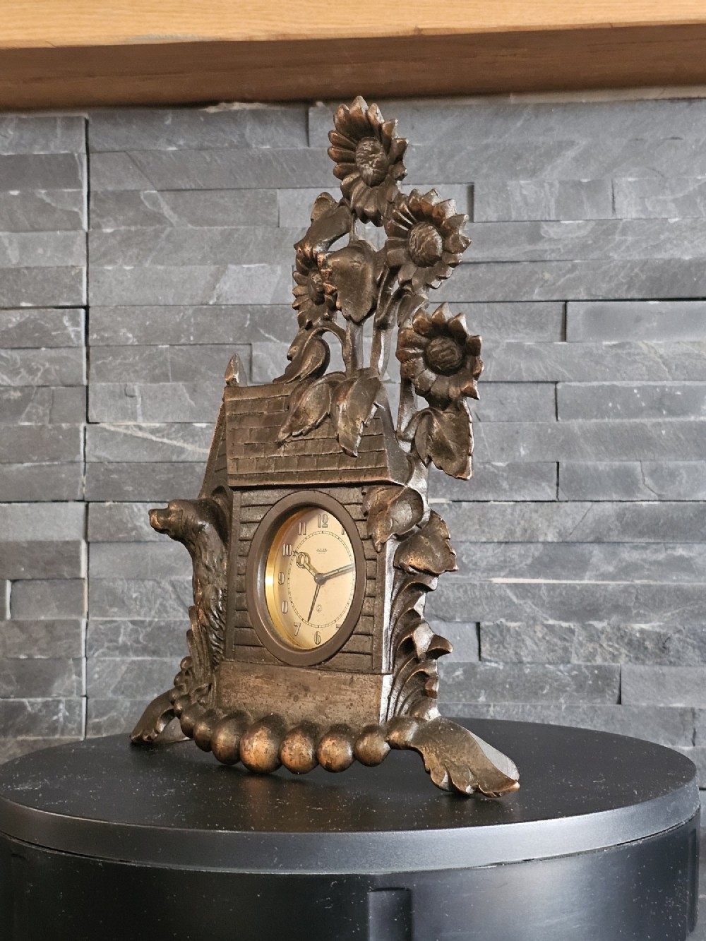 A bronzed Art Deco table clock shaped like a dog kennel with sunflowers on top and a dog figure on the left side of the circular dial. View III