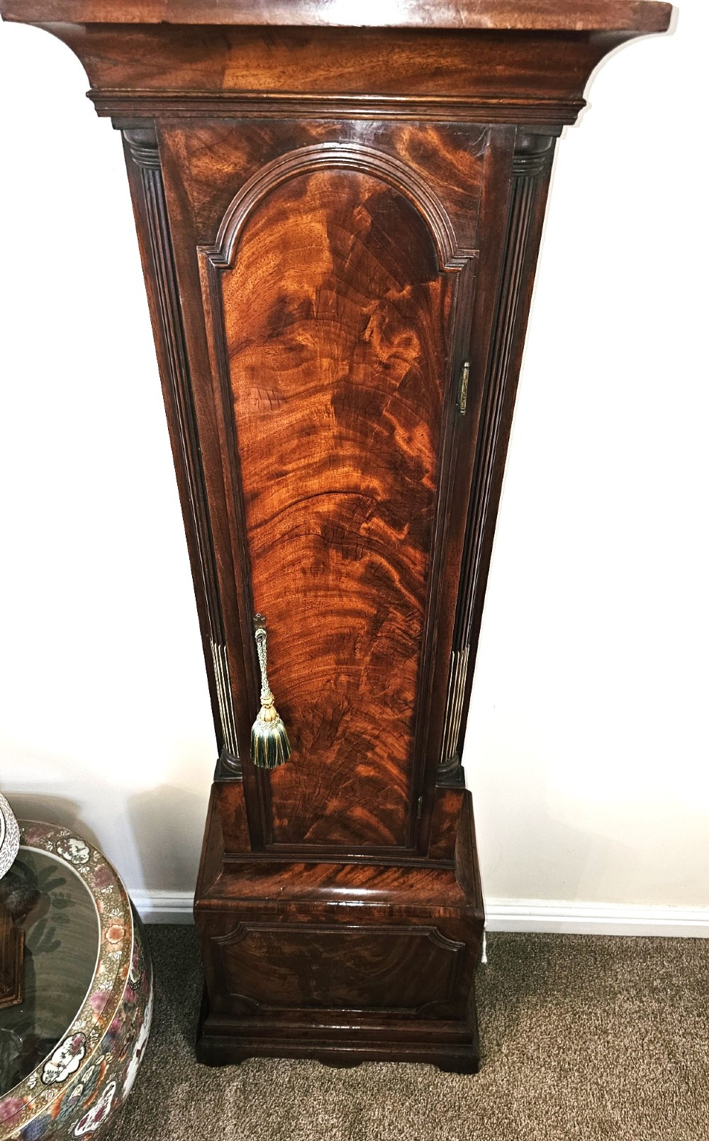 A Georgian flame mahogany longcase clock featuring an arched hood with brass-capped fluted columns, an engraved brass dial with Roman numerals, and a trunk door showcasing rich wood grain. View III