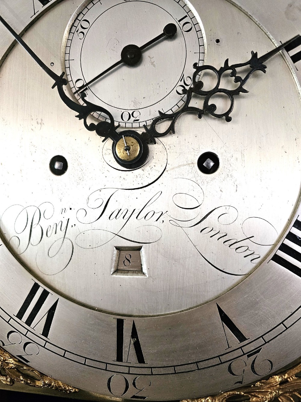 A Georgian flame mahogany longcase clock featuring an arched hood with brass-capped fluted columns, an engraved brass dial with Roman numerals, and a trunk door showcasing rich wood grain. View VI