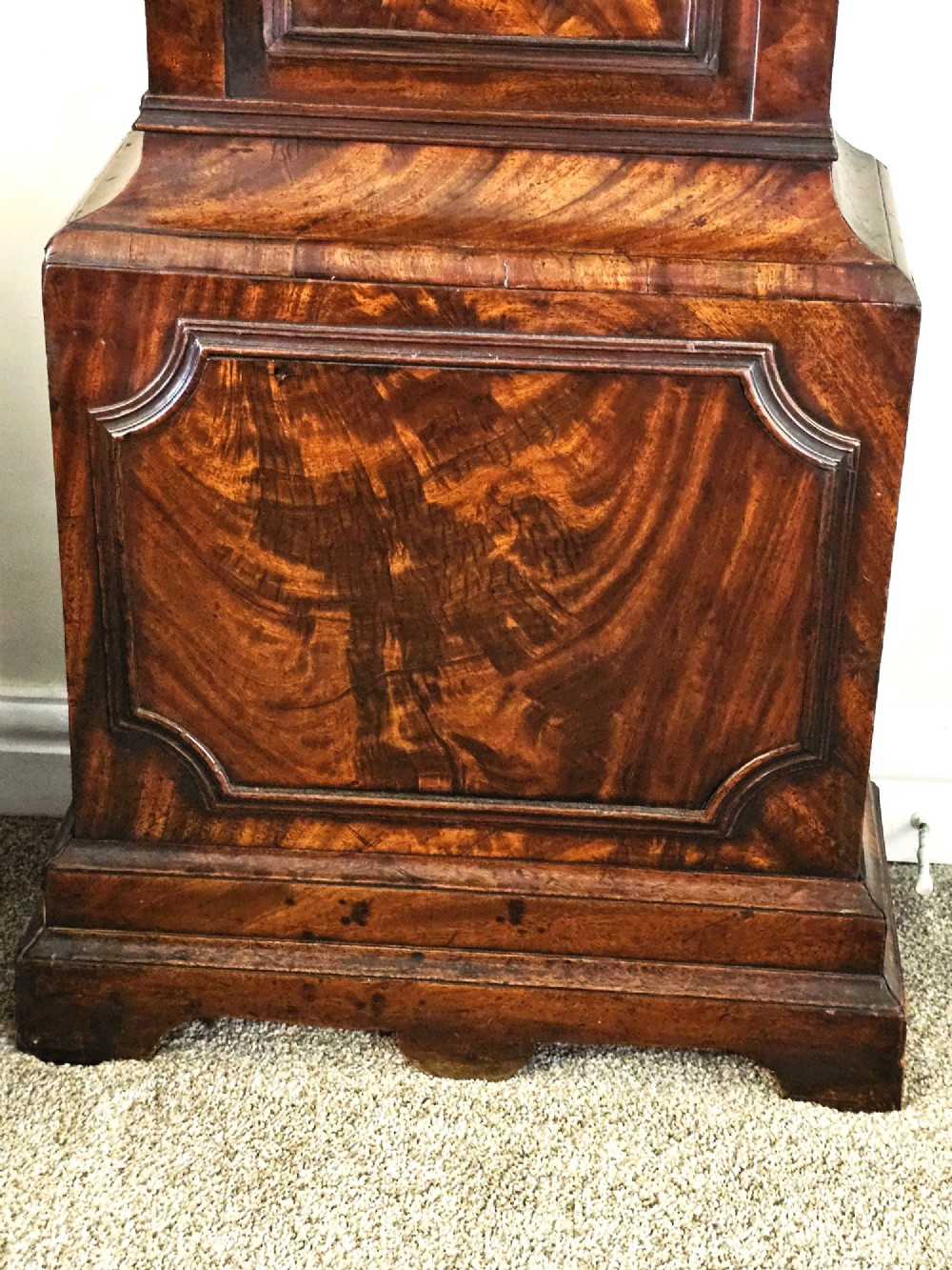 A Georgian flame mahogany longcase clock featuring an arched hood with brass-capped fluted columns, an engraved brass dial with Roman numerals, and a trunk door showcasing rich wood grain. View XII
