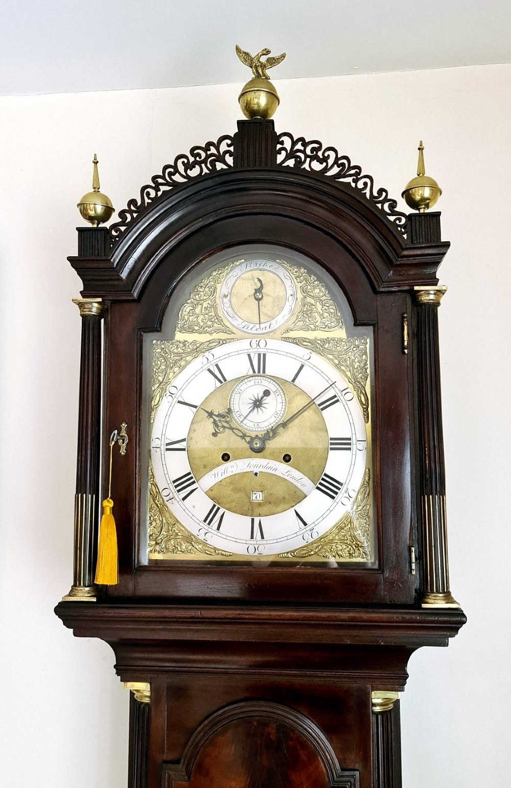 A late 18th-century Georgian mahogany longcase clock with an arched brass dial, flame mahogany trunk door, and pediment hood topped with three brass finials. View II