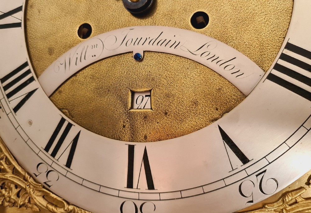 A late 18th-century Georgian mahogany longcase clock with an arched brass dial, flame mahogany trunk door, and pediment hood topped with three brass finials. View VI