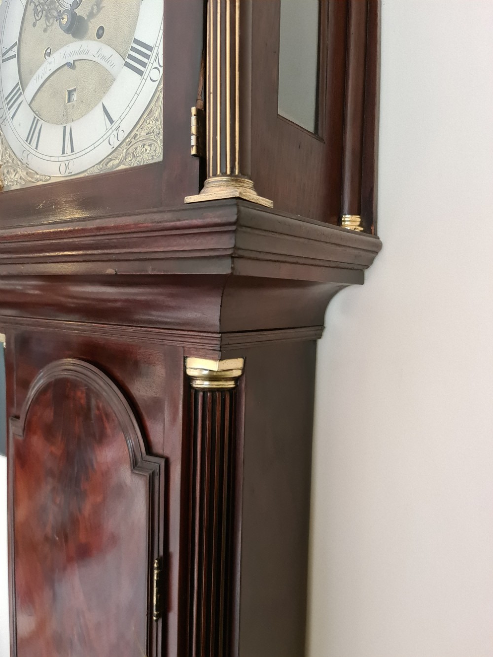 A late 18th-century Georgian mahogany longcase clock with an arched brass dial, flame mahogany trunk door, and pediment hood topped with three brass finials. View VII
