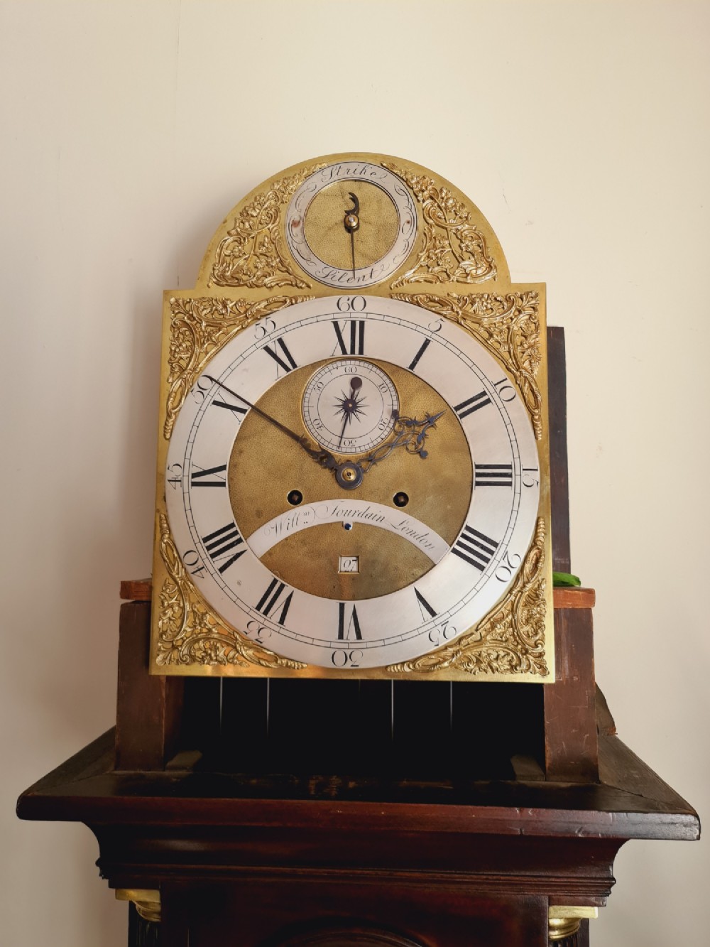 A late 18th-century Georgian mahogany longcase clock with an arched brass dial, flame mahogany trunk door, and pediment hood topped with three brass finials. View VIII