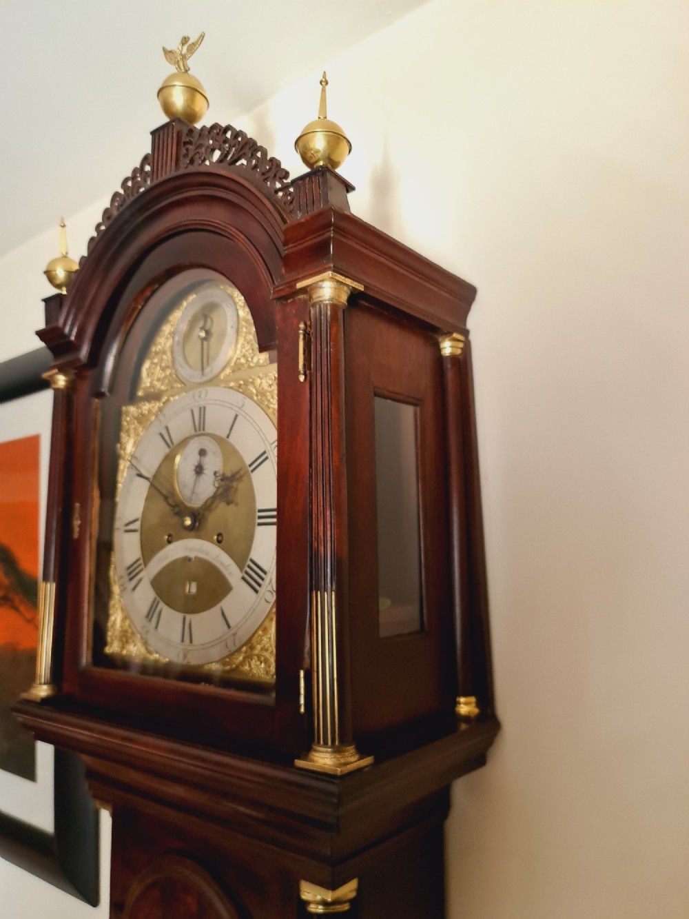 A late 18th-century Georgian mahogany longcase clock with an arched brass dial, flame mahogany trunk door, and pediment hood topped with three brass finials. View IX