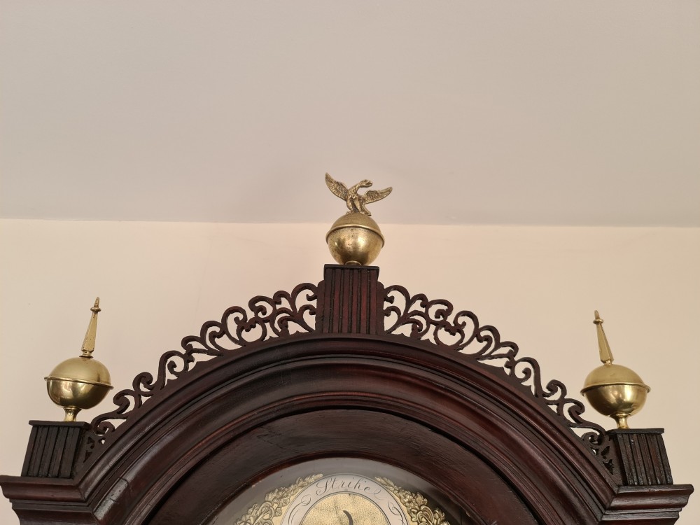 A late 18th-century Georgian mahogany longcase clock with an arched brass dial, flame mahogany trunk door, and pediment hood topped with three brass finials. View X