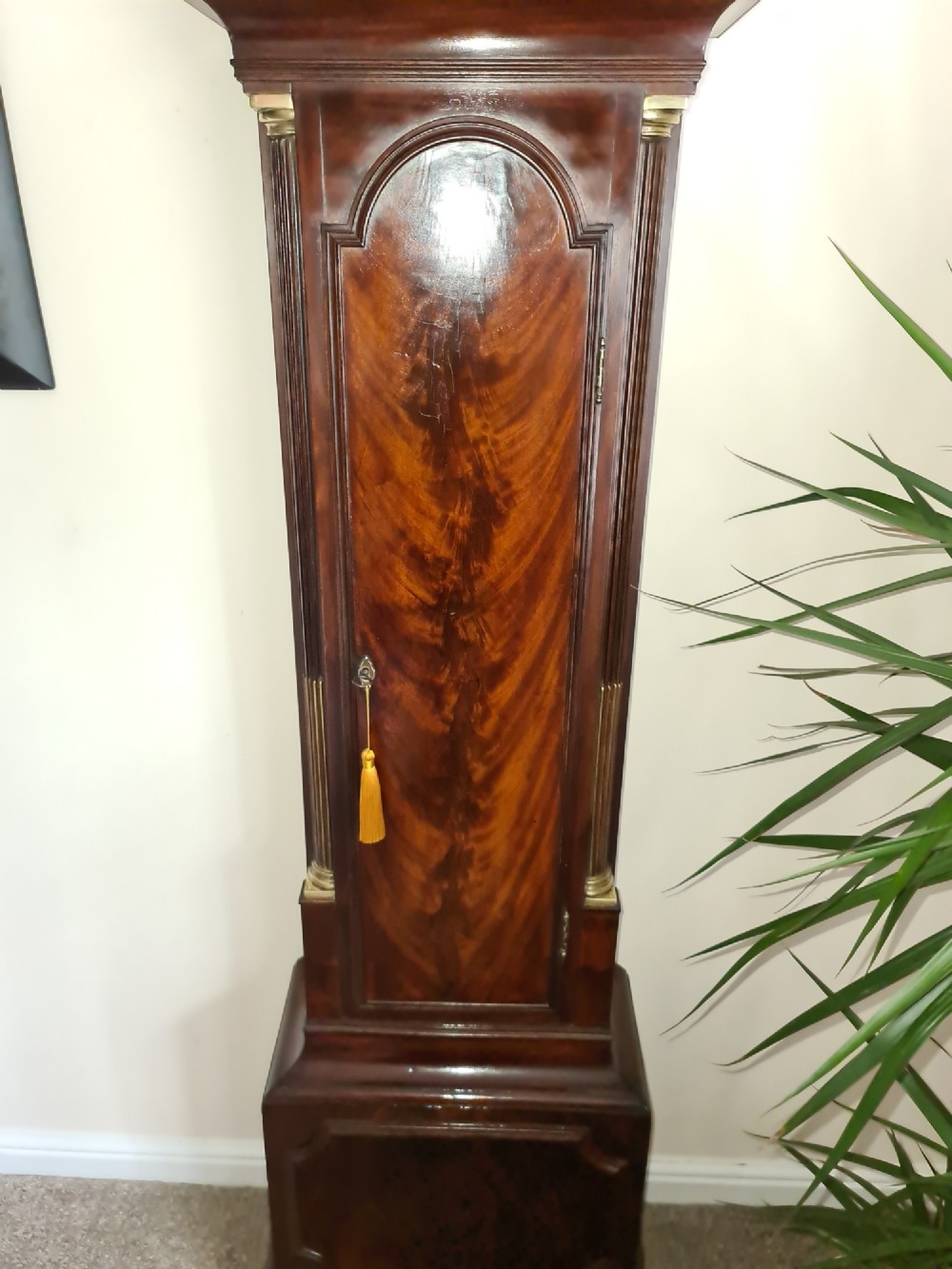 A late 18th-century Georgian mahogany longcase clock with an arched brass dial, flame mahogany trunk door, and pediment hood topped with three brass finials. View XI