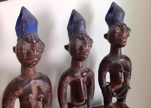 fig 1. Three hand-carved dark wood Yoruba Ere Ibeji figures featuring tall indigo-pigmented coiffures, carved facial scarification, and glass waist beads.