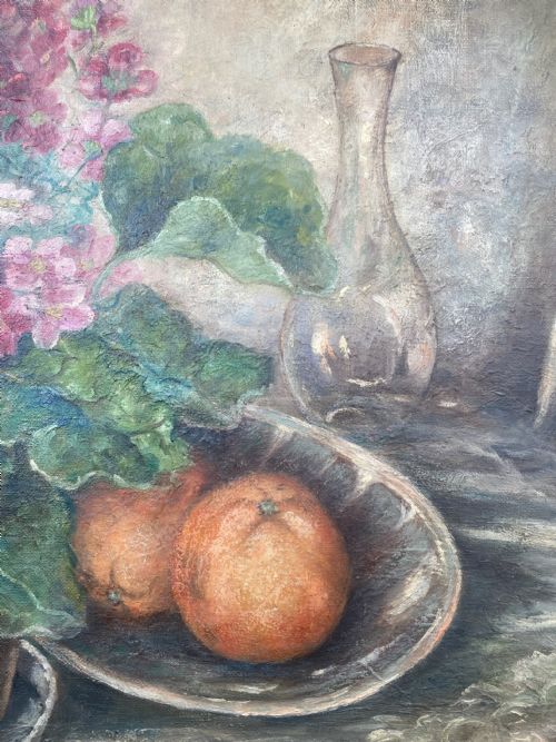 fig 1. A framed 1934 still life oil painting on canvas depicting a potted pink geranium, two oranges in a dish, and a glass vessel on a table.