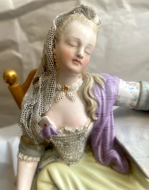 fig 1. A 19th-century Meissen hard-paste porcelain figurine depicting a sleeping woman in 18th-century dress with applied lace, seated in a chair beside a table.