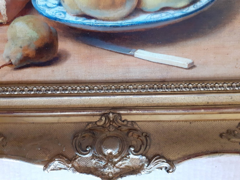 A mid-19th-century oil painting on canvas depicting a rustic still life with bread, fruit on a ceramic plate, a pear, and a knife, housed in an ornate carved gold frame. View V