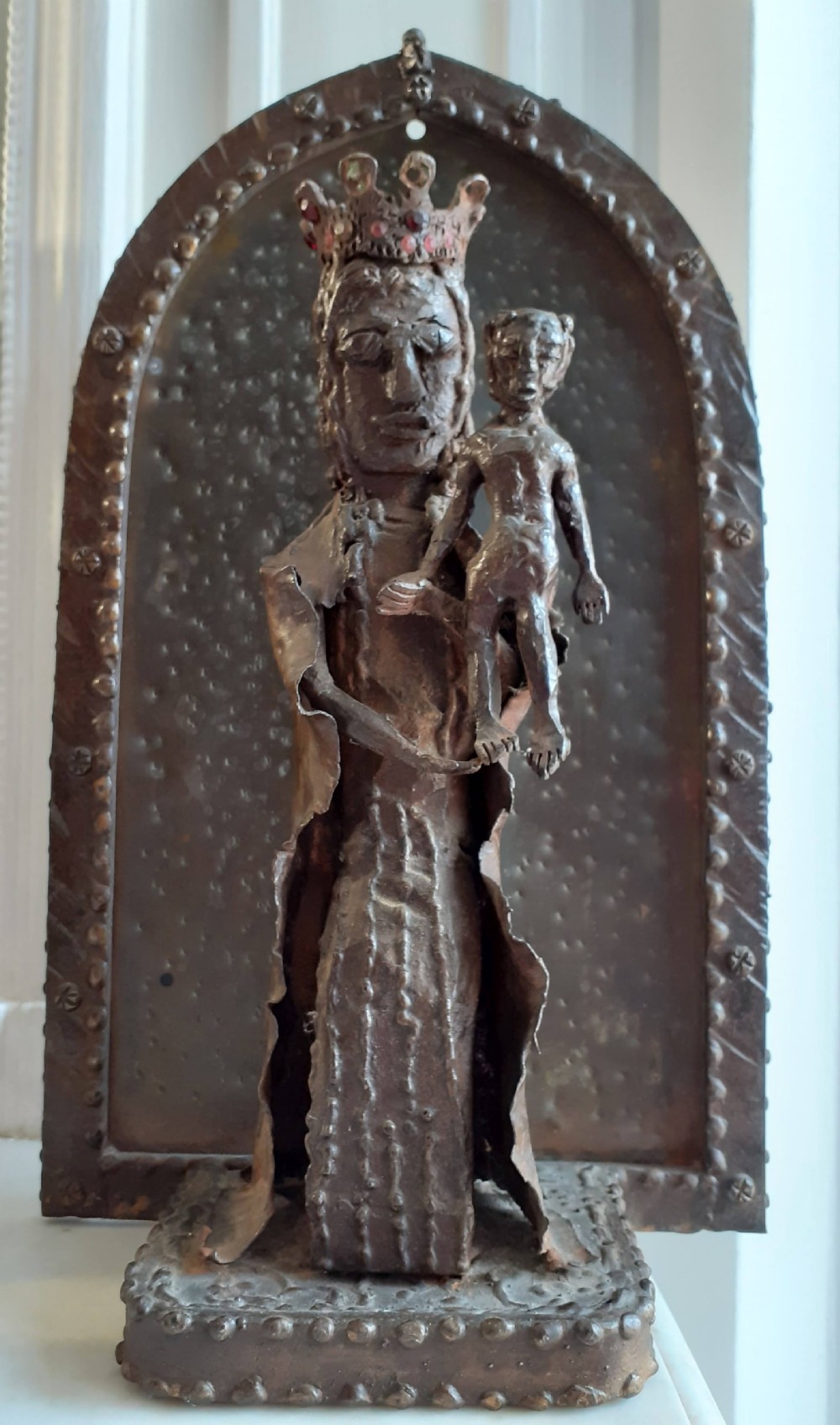 A hand-wrought metal sculpture depicting a crowned Madonna holding the Christ Child within an arched backdrop.