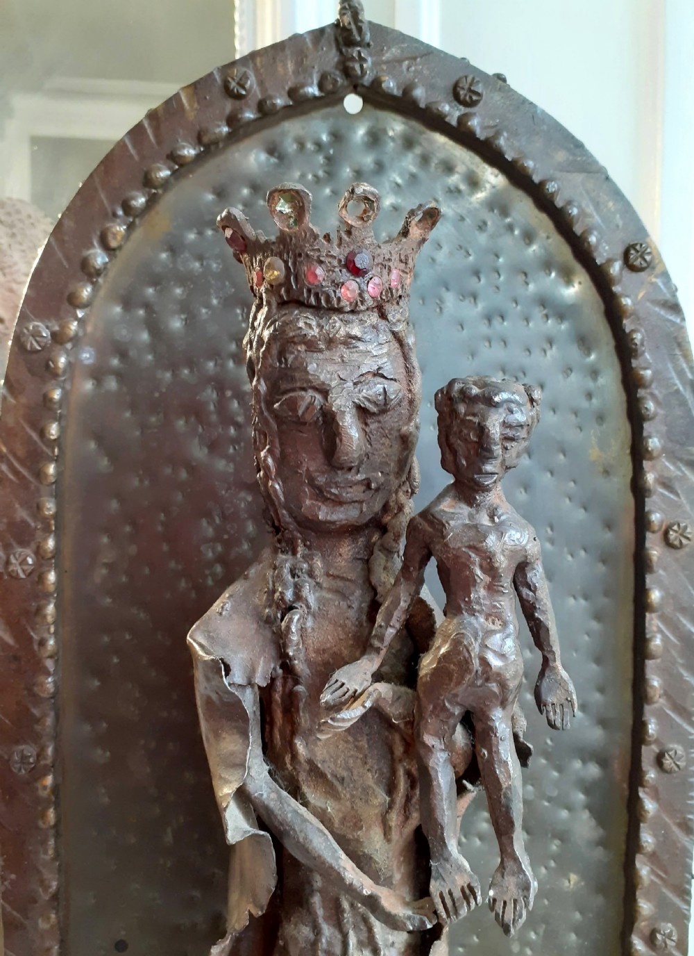 A hand-wrought metal sculpture depicting a crowned Madonna holding the Christ Child within an arched backdrop. View III