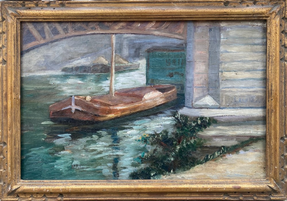An impressionist oil painting depicting a wooden boat moored along the River Seine under a stone bridge, presented in a carved gilded frame.