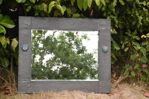 fig 1. A rectangular Arts and Crafts wall mirror featuring a hammered pewter metal frame decorated with corner rivets and two circular turquoise ceramic cabochons on the side borders.