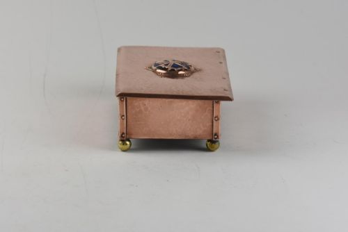 fig 1. A rectangular hand-hammered copper box featuring brass ball feet, riveted corners, and a central blue enamel cabochon with a pierced butterfly overlay on the lid.