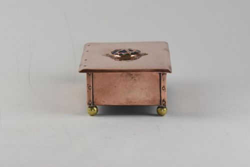 fig 3. A rectangular hand-hammered copper box featuring brass ball feet, riveted corners, and a central blue enamel cabochon with a pierced butterfly overlay on the lid.