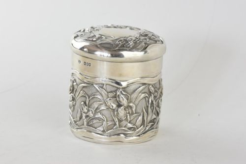 fig 1. A cylindrical Art Nouveau sterling silver box with a fitted lid, decorated with raised repousse iris motifs.