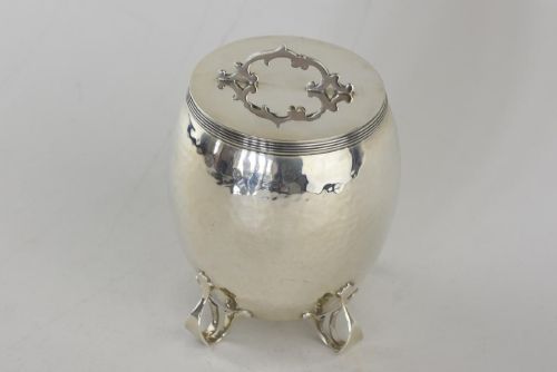 fig 1. An Arts and Crafts hammered sterling silver tea caddy featuring a planished surface, looped feet, and a flat lid with a scrolled handle.