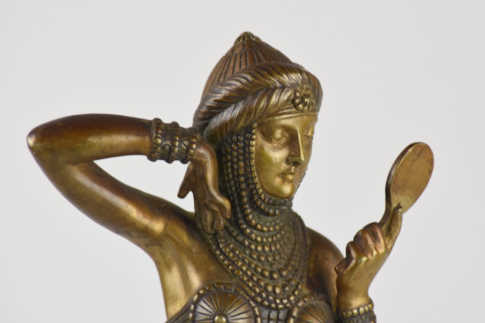 An Art Deco bronze figure depicting a female dancer in theatrical attire holding a small hand mirror, mounted on a square onyx plinth. View VIII