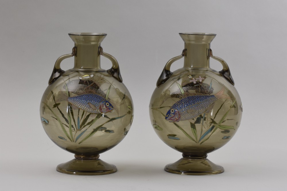 Pair of translucent smoky brown glass vases featuring twin loop handles, pedestal bases, and hand-painted enamelled motifs of blue fish and water plants.
