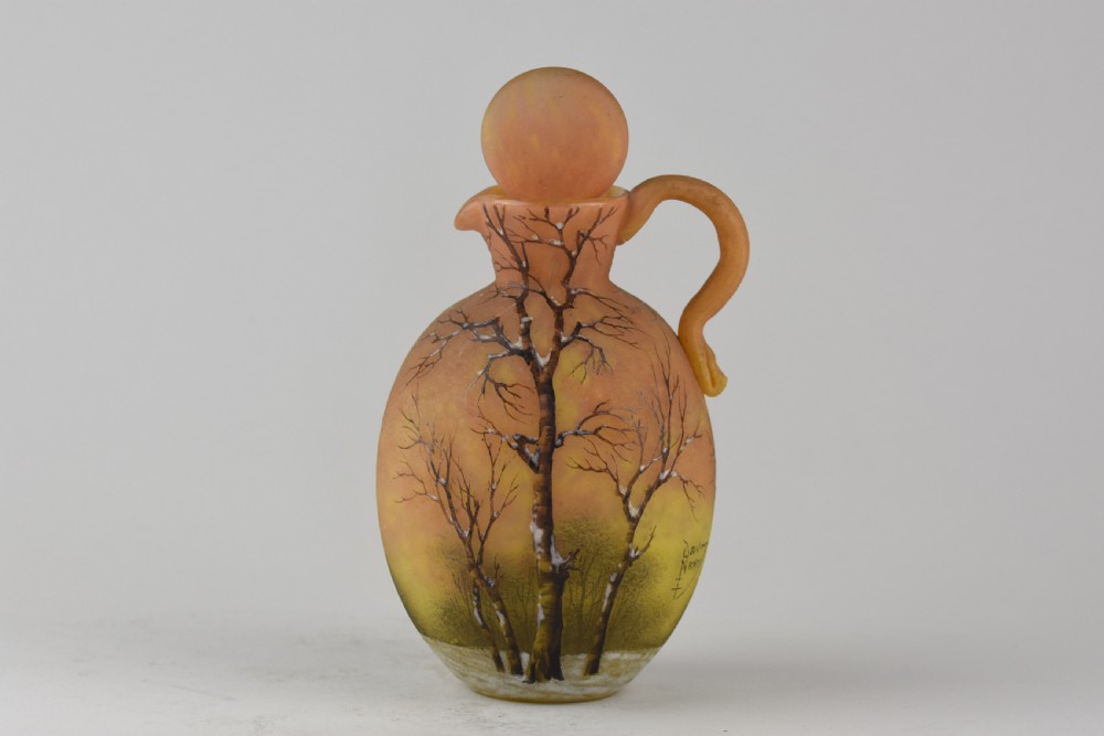 An Art Nouveau Daum Nancy glass jug featuring acid-etched and enamelled winter landscape decoration on an orange gradient background, complete with a spherical stopper.