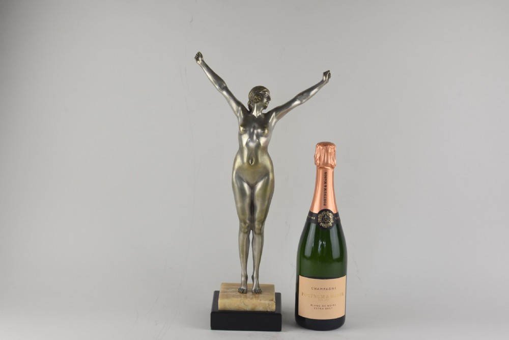 An Art Deco silvered bronze sculpture depicting a nude female figure with raised arms standing atop a tiered marble and black base. View II