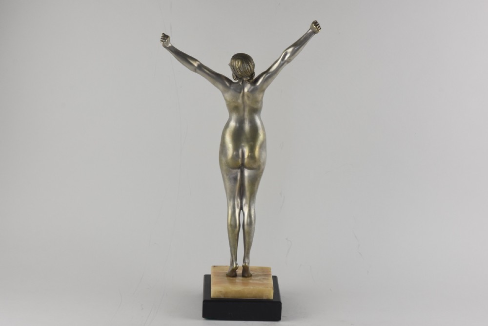 An Art Deco silvered bronze sculpture depicting a nude female figure with raised arms standing atop a tiered marble and black base. View V