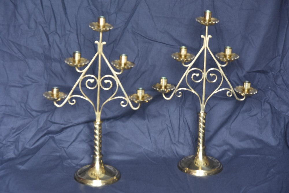 A pair of Arts and Crafts five-light brass candelabra featuring openwork scroll framing, twisted stems, and circular stepped bases.
