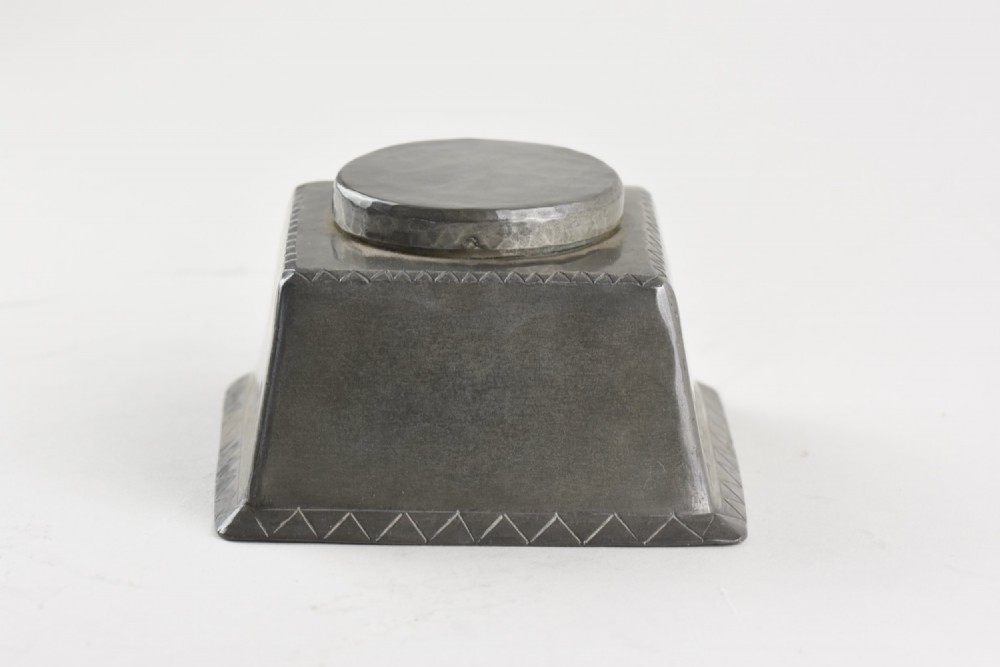A square tapered hand-hammered pewter inkwell featuring a circular lid and stamped chevron borders around the edges.