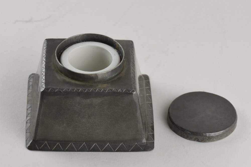 A square tapered hand-hammered pewter inkwell featuring a circular lid and stamped chevron borders around the edges. View II