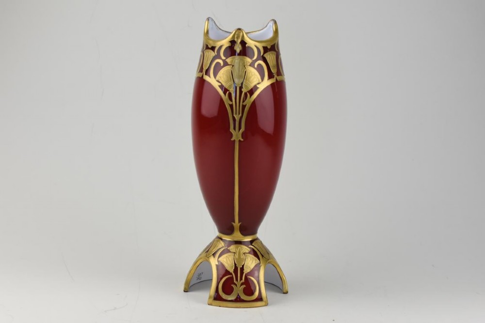 An Art Nouveau deep red glass vase with gilded enamel lotus motifs, featuring a shaped rim and a four-footed base.