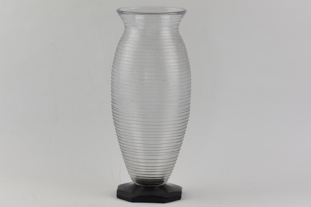 A ribbed grey glass vase with a flared rim resting on an octagonal black base.