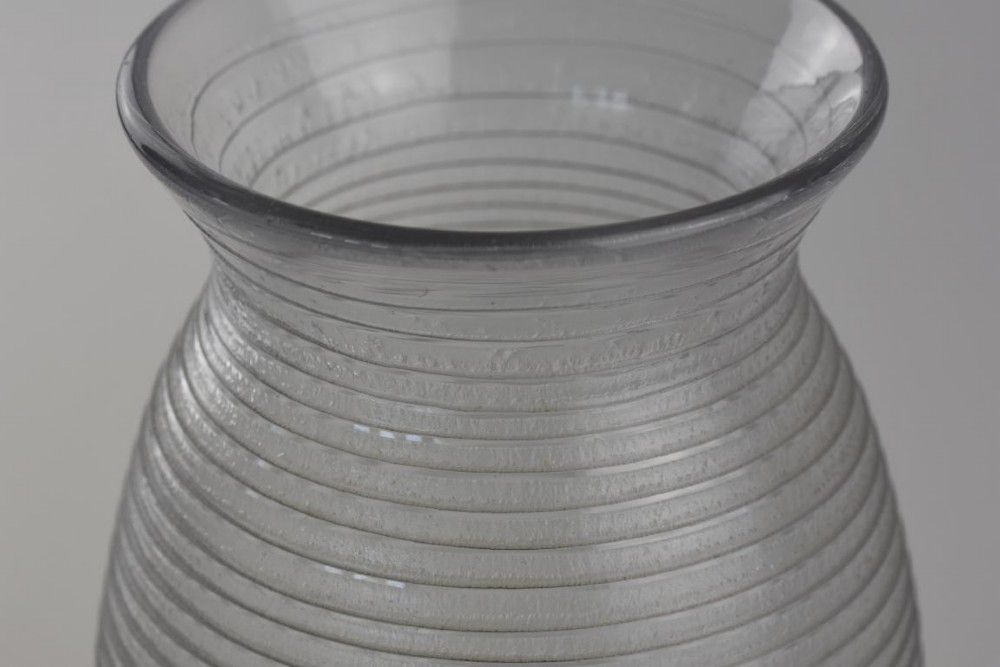 A ribbed grey glass vase with a flared rim resting on an octagonal black base. View V