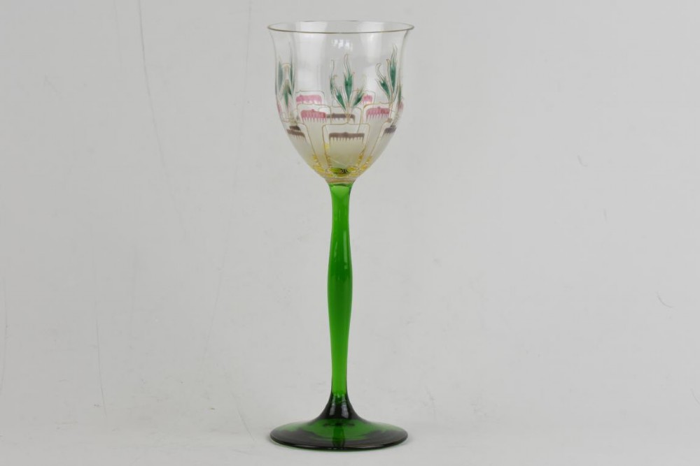 An Art Nouveau wine glass featuring an elongated green stem and a clear bowl decorated with pink and green enamelled floral motifs.