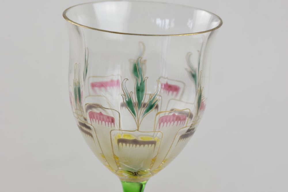 An Art Nouveau wine glass featuring an elongated green stem and a clear bowl decorated with pink and green enamelled floral motifs. View II