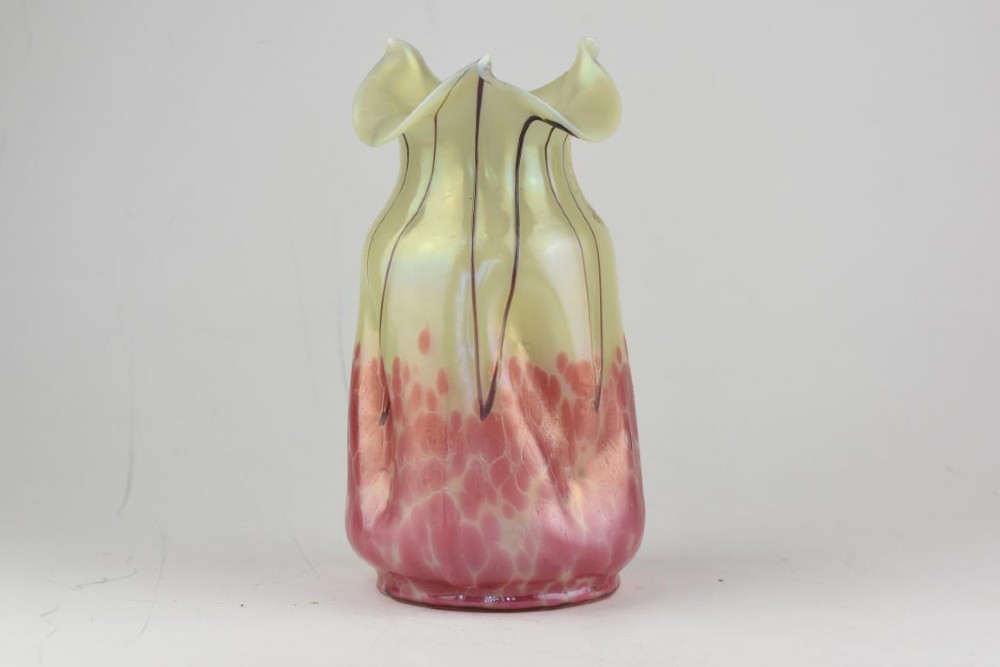 An Art Nouveau iridescent glass vase featuring a pale yellow upper section with dark glass trailing and a speckled pink lower base with a ruffled rim.