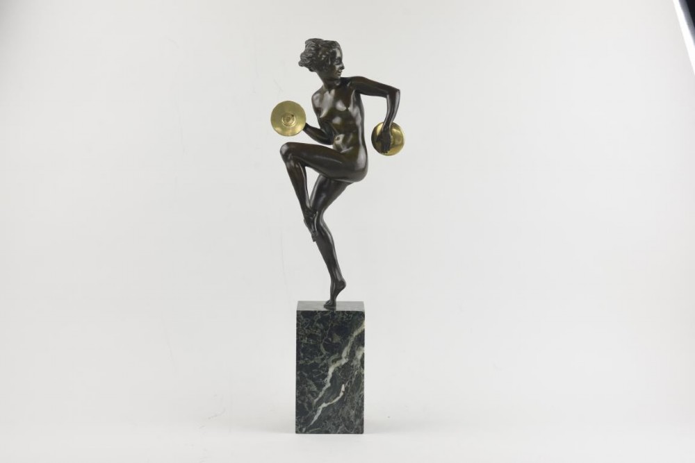 An Art Deco dark patinated bronze figure of a female dancer holding cymbals, balanced on one leg atop a tall green-veined marble base.