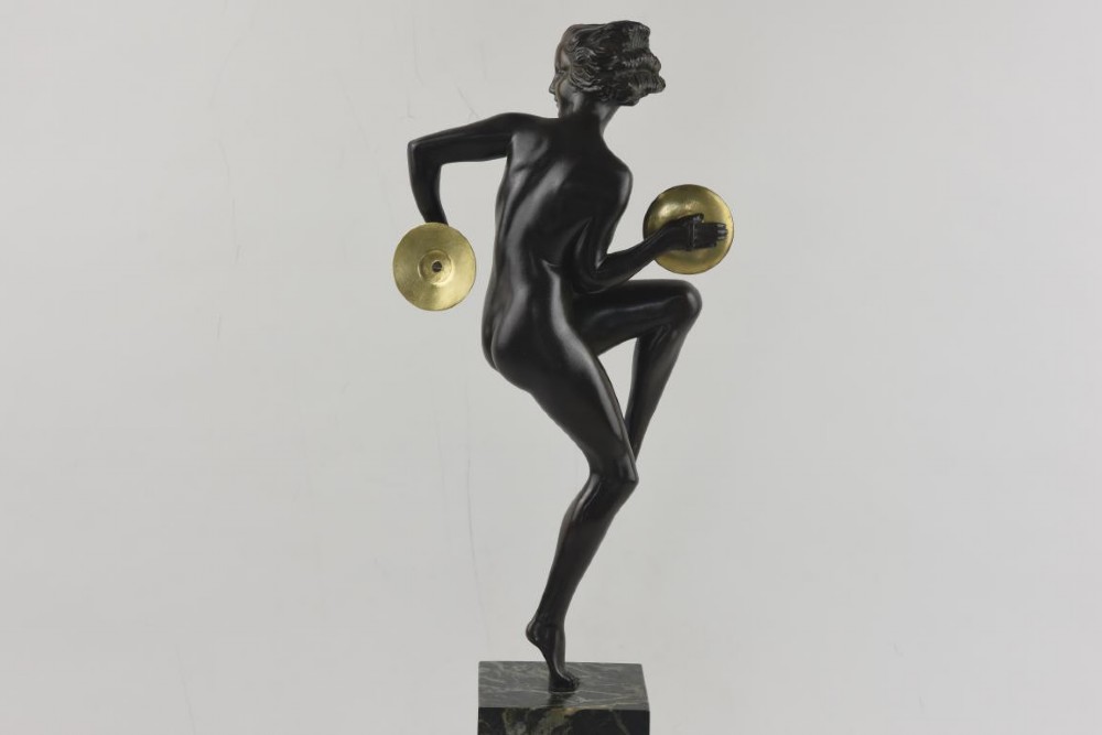 An Art Deco dark patinated bronze figure of a female dancer holding cymbals, balanced on one leg atop a tall green-veined marble base. View IV