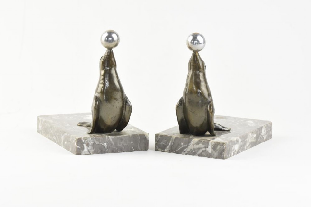A pair of Art Deco metal sea lions balancing chrome spheres on their noses, mounted on rectangular grey marble bases. View II