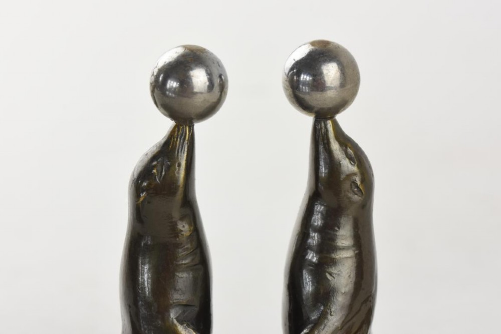 A pair of Art Deco metal sea lions balancing chrome spheres on their noses, mounted on rectangular grey marble bases. View IV