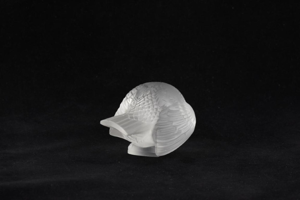 A clear frosted glass sculpture depicting a small sparrow with its head lowered in a shy pose against a black background. View II