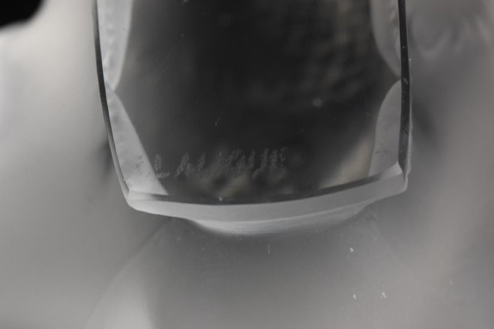 A clear frosted glass sculpture depicting a small sparrow with its head lowered in a shy pose against a black background. View IV