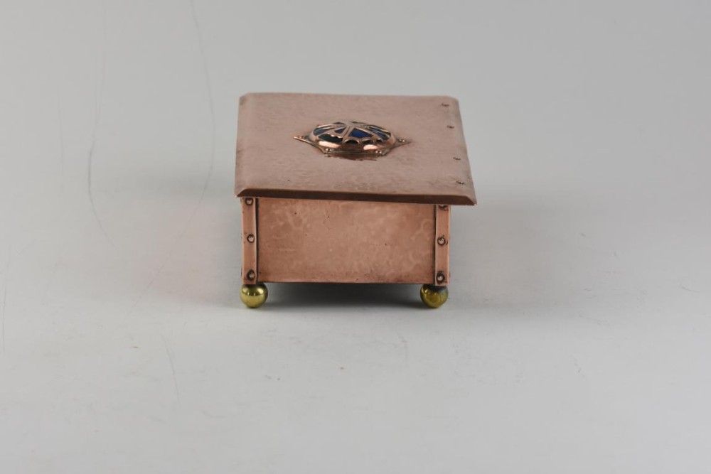 A rectangular hand-hammered copper box featuring brass ball feet, riveted corners, and a central blue enamel cabochon with a pierced butterfly overlay on the lid. View II