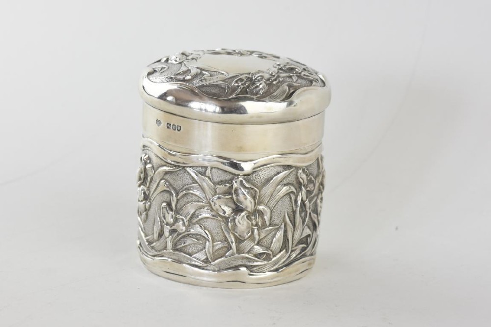 A cylindrical Art Nouveau sterling silver box with a fitted lid, decorated with raised repousse iris motifs. View II