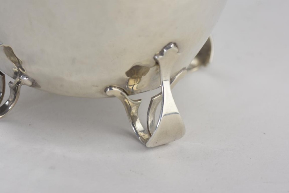 An Arts and Crafts hammered sterling silver tea caddy featuring a planished surface, looped feet, and a flat lid with a scrolled handle. View VII