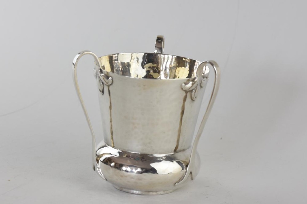 A hand-hammered silver three-handled tyg cup with a planished finish and stylized handle mounts.