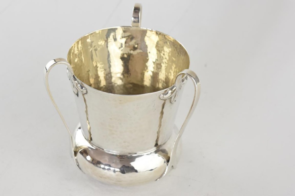 A hand-hammered silver three-handled tyg cup with a planished finish and stylized handle mounts. View II