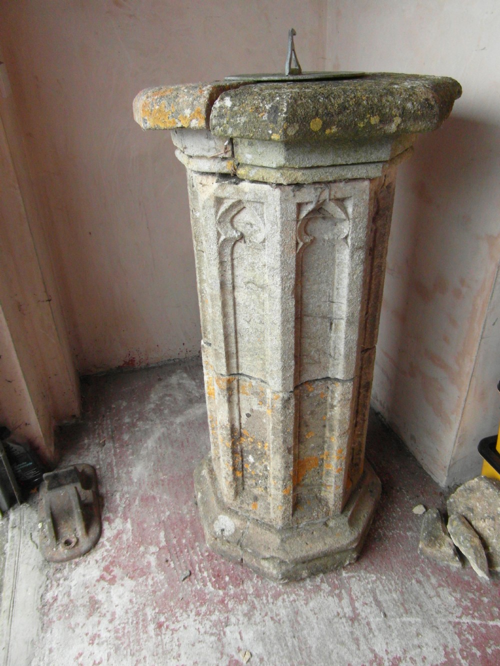 An octagonal carved grey stone sundial plinth featuring Gothic blind tracery panels topped with a circular dial.